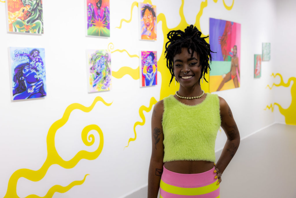 Artist Mithsuca Berry stands in front of their artwork at the opening of their exhibition, The Sun Knows No Impostor.