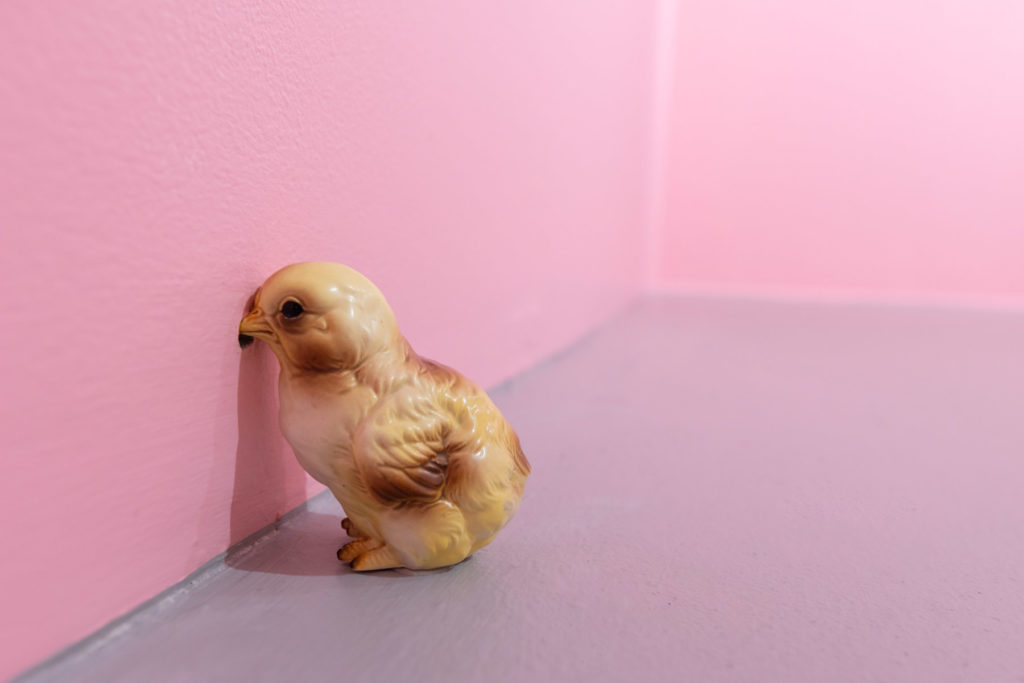 A small yellow ceramic chick faces the wall. Installation view of Catalina Schliebener: Growing Sideways at the Boston Center for the Arts. (2021) Photo by Melissa Blackall