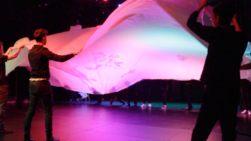 A group of people are handling a light-up parachute, similar to a scene from elementary school gym.