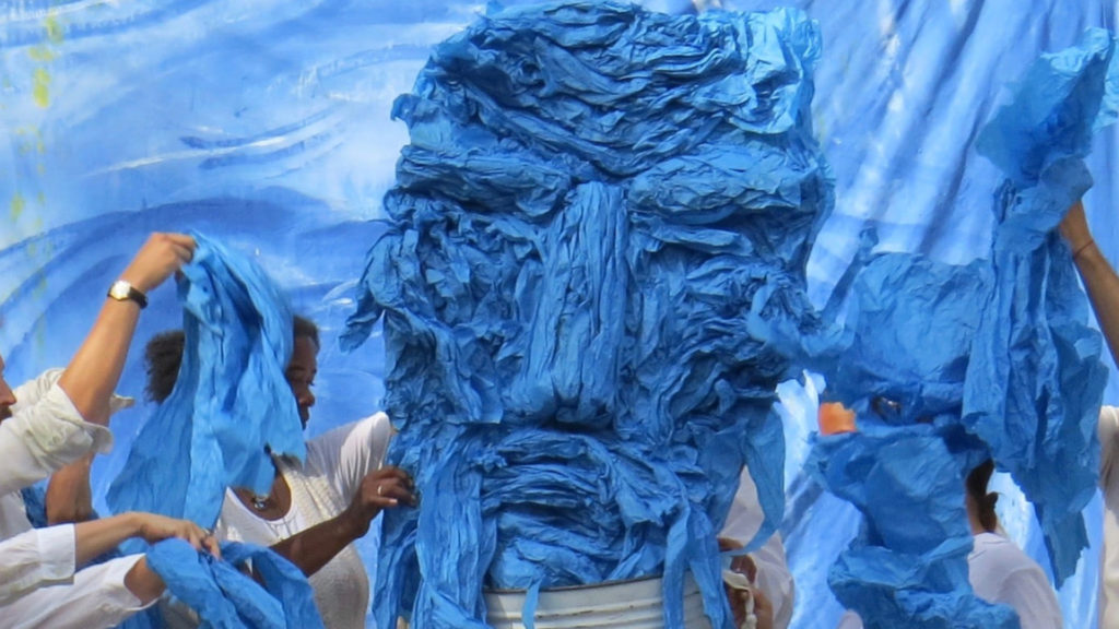 People are putting what looks like blue tissue paper into a bucket.